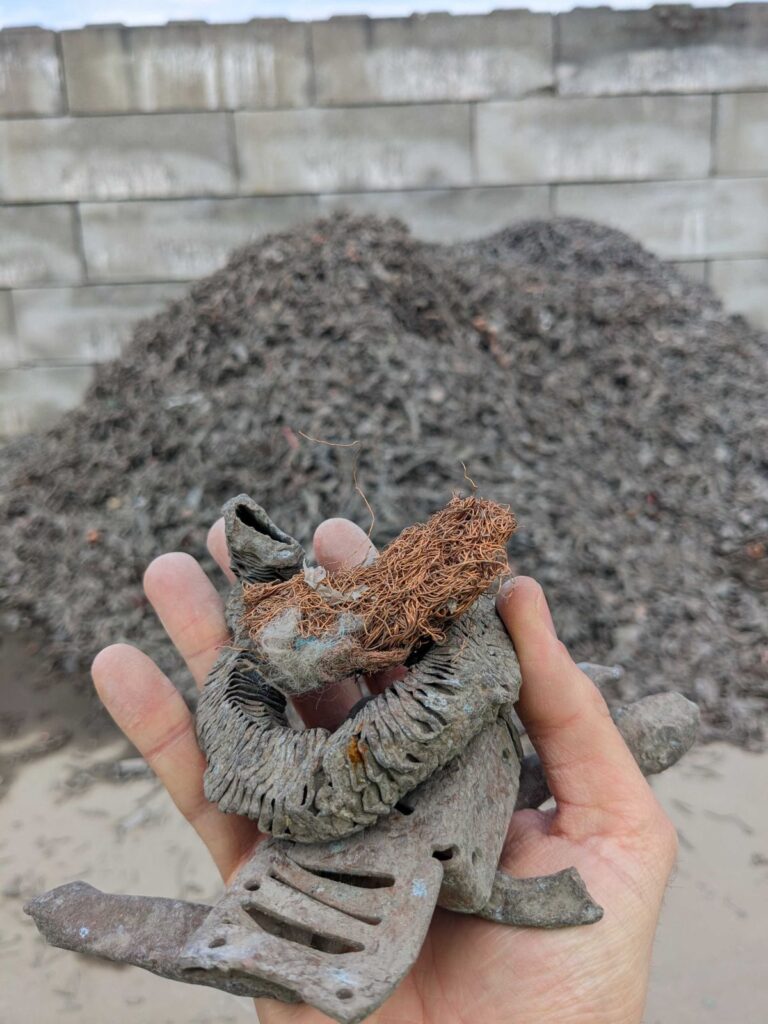A hand holding a copper winding in front of a heap of shredded steel